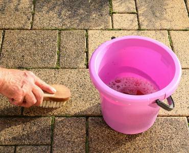 Person cleaning a stone terrace with a brush and soapy water