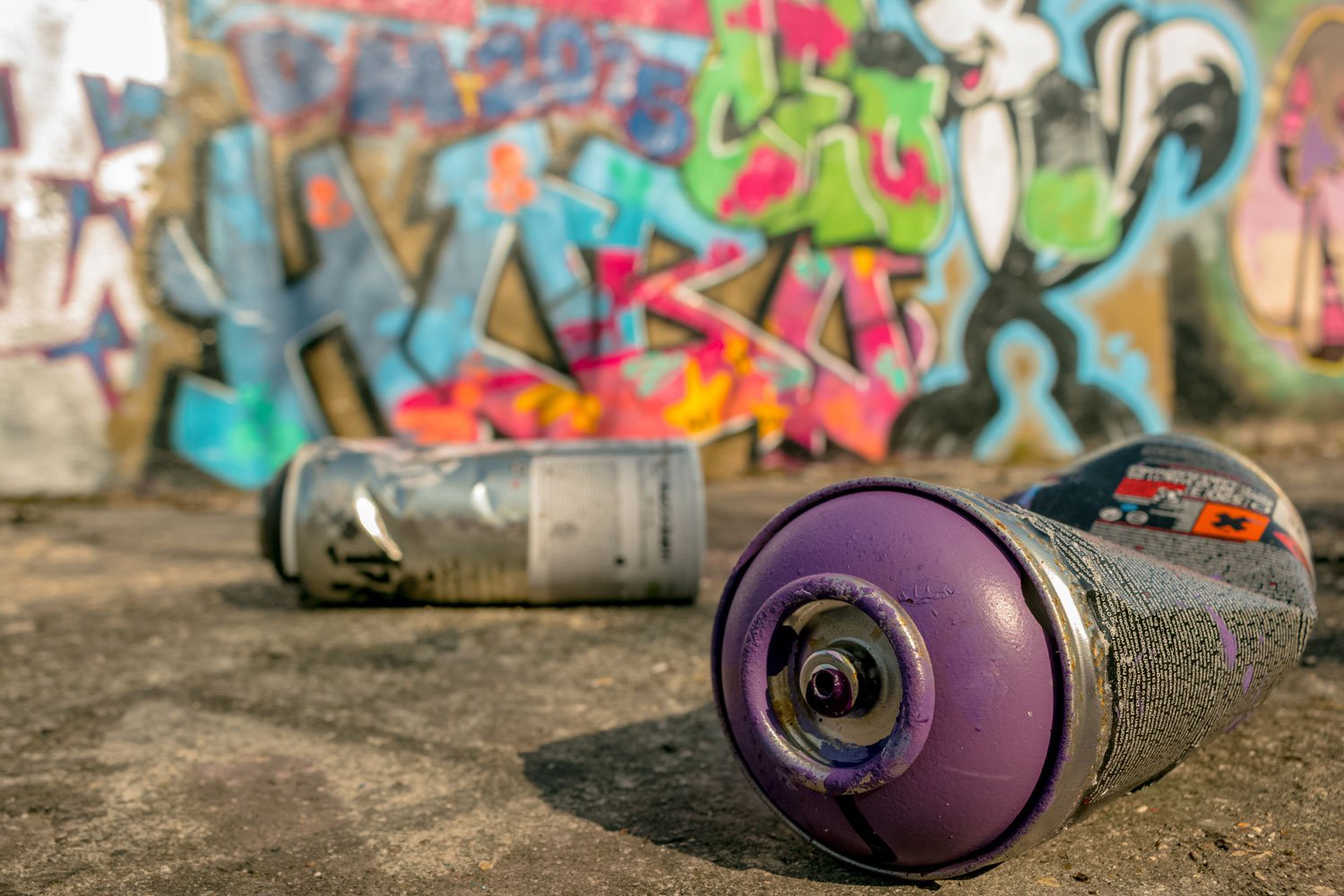 Discarded spray pain cans in front of graffiti