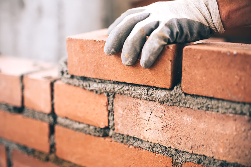 A worker placing a brick on mortar