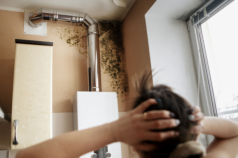 A woman looking at her mould-covered wall in shock