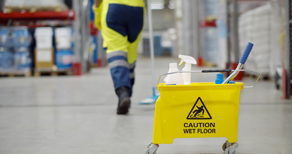 Cropped shot of janitor with bucket washing floor in warehouse