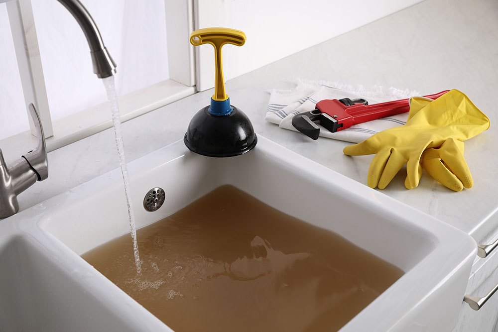 Kitchen counter with clogged sink, plunger and plumber's accessories