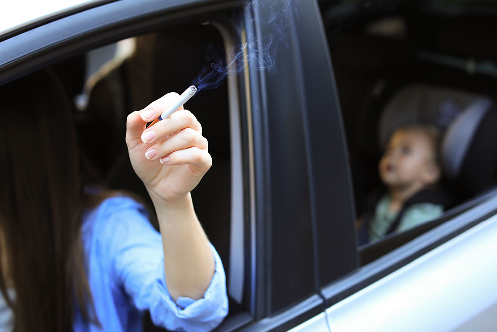 An adult smoking in the car with her infant