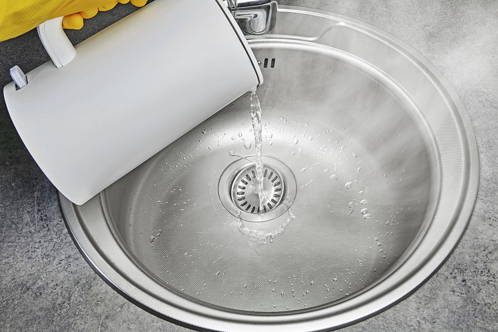 Someone pouring hot water from a kettle down a sink drain