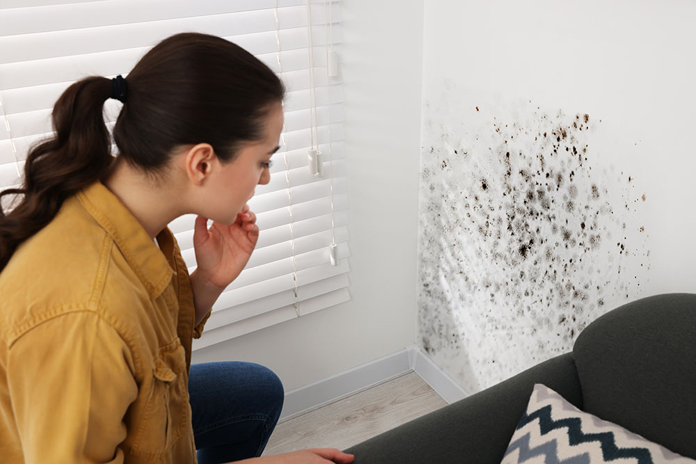 A woman looking at a wall covered in mould