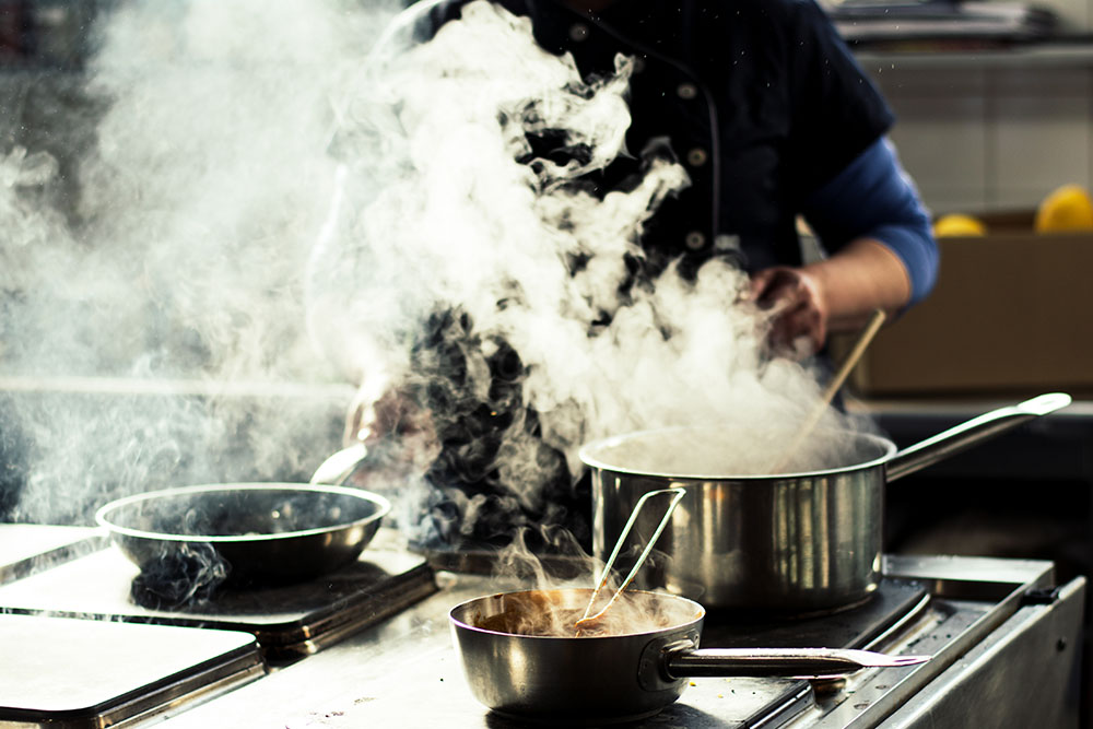 Kitchen staff next to a pot producing smoke