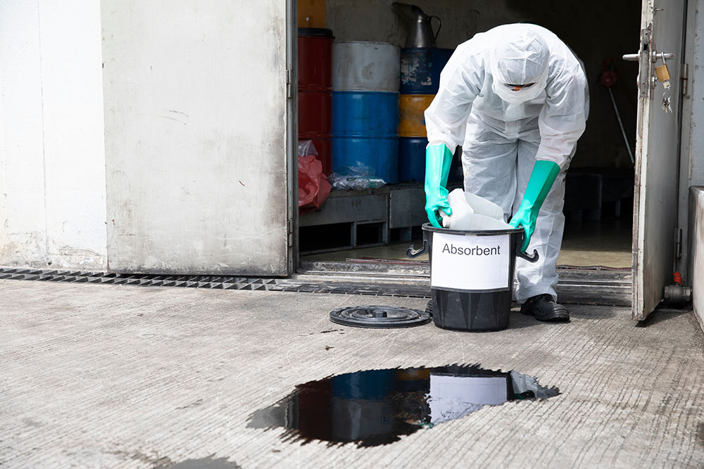 Man in PPE cleaning an oil spill with absorbent materials