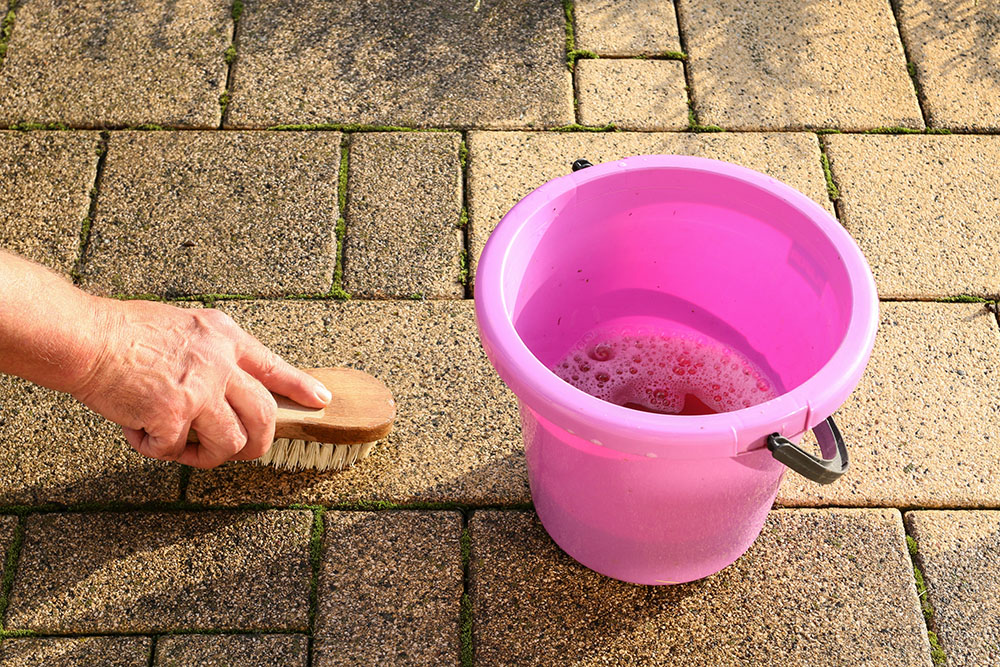 Person cleaning a stone terrace with a brush and soapy water