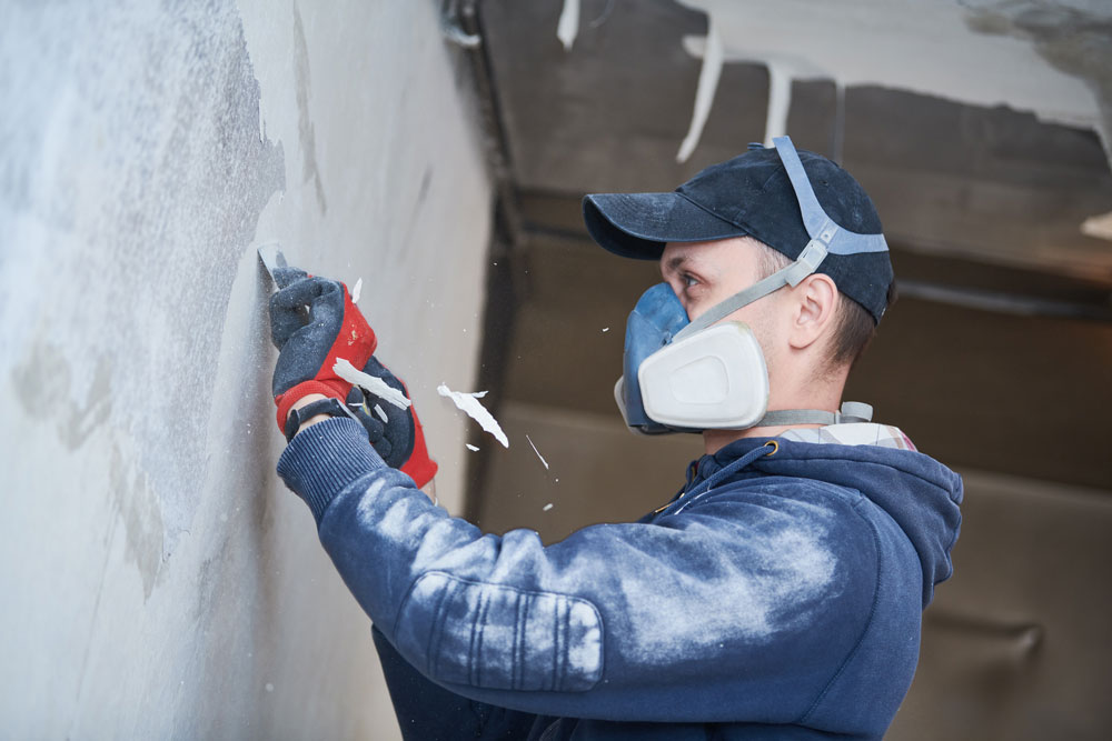 Decorator removing damaged paint from wall