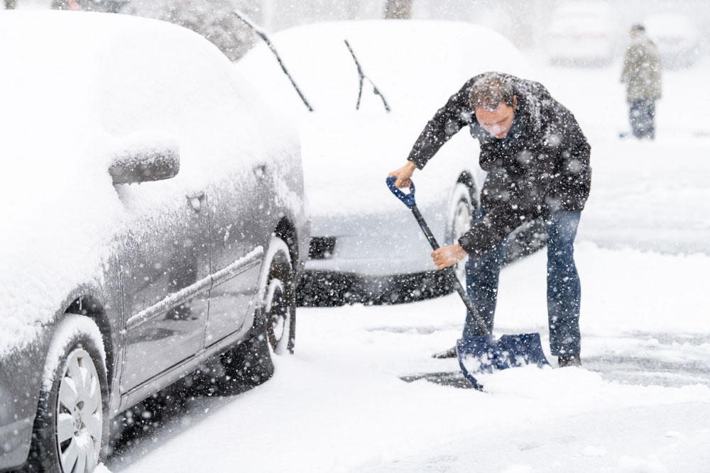 man shovelling snow away from car