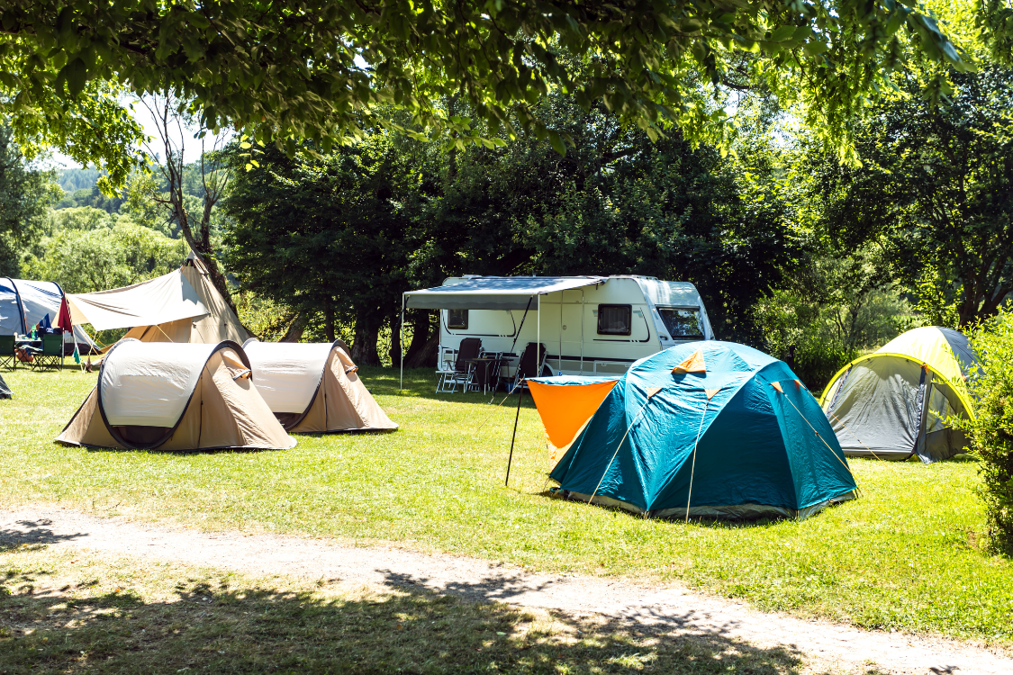 A camping ground with tents and a camper van with an awning set up